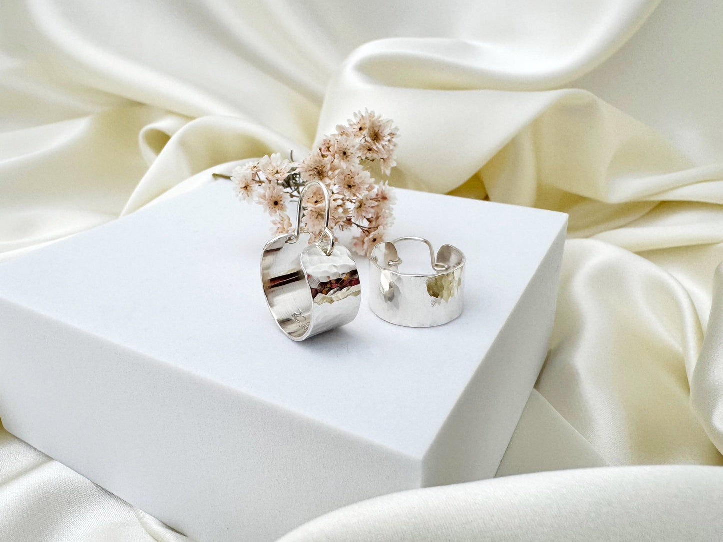 Silver hoop earrings with dried flowers on a white surface with beige fabric background