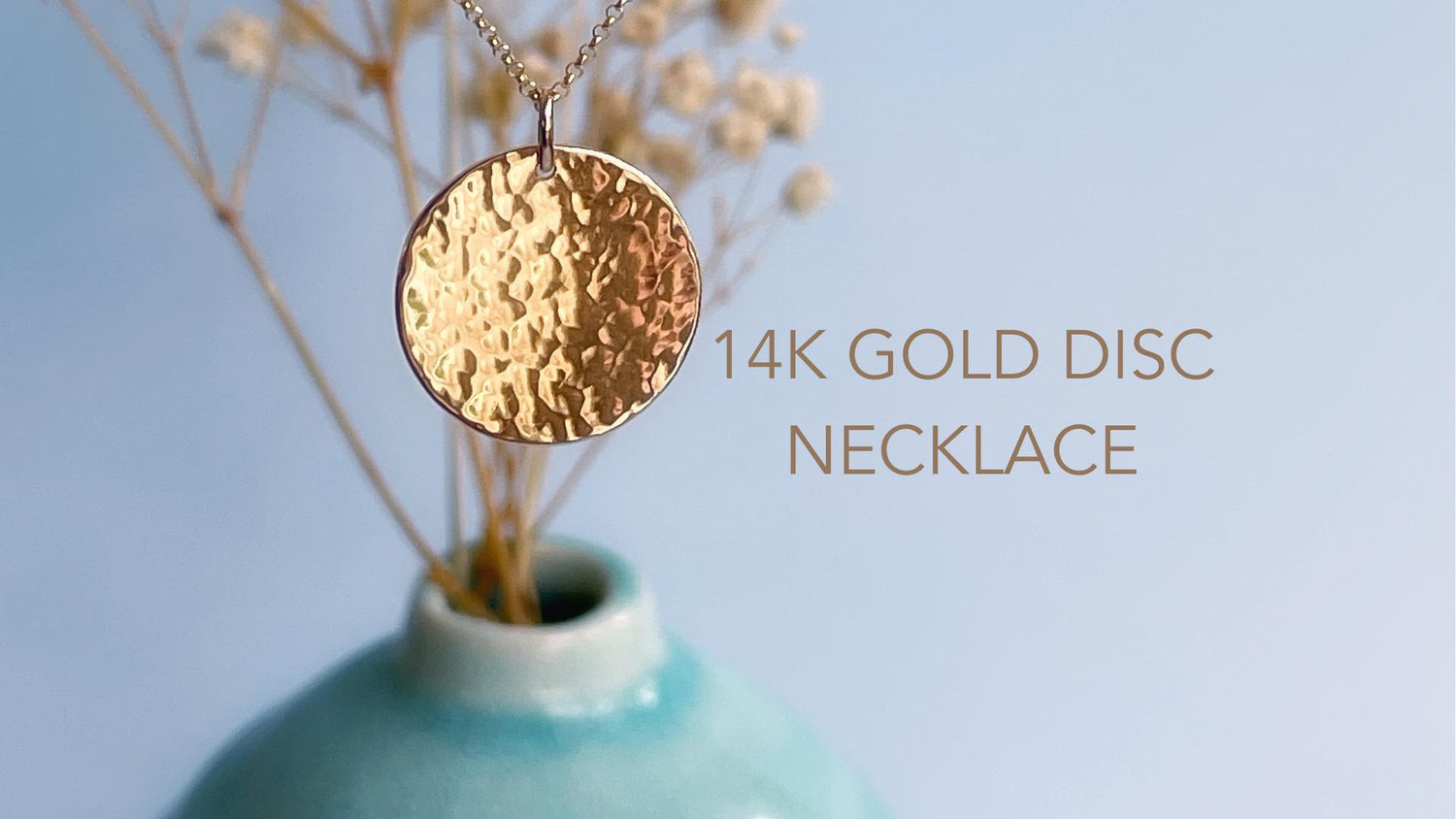 A solid 14k yellow gold hammered disc pendant hanging from a fine gold necklace.