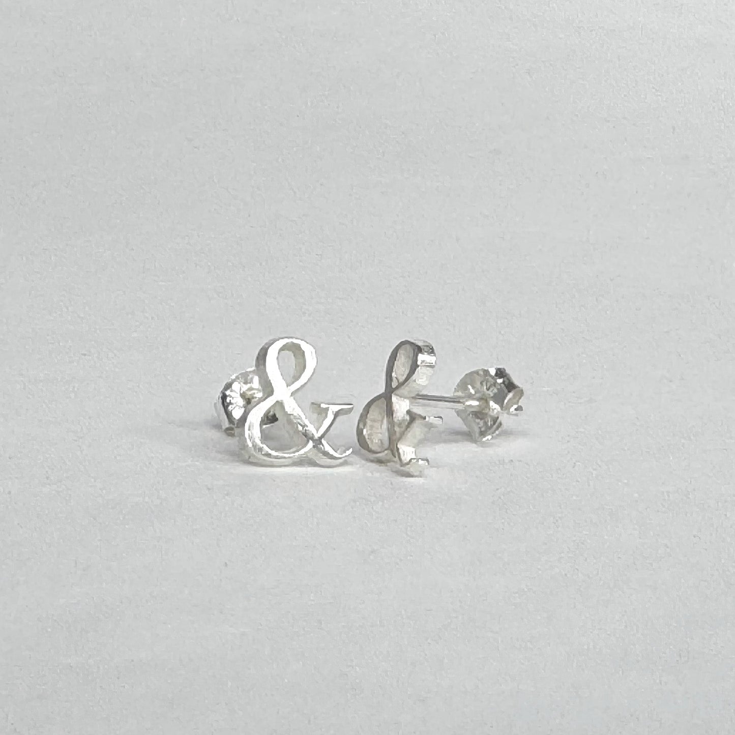 Sterling silver stud earrings shaped like ampersands on a light grey background