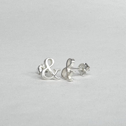Sterling silver stud earrings shaped like ampersands on a light grey background
