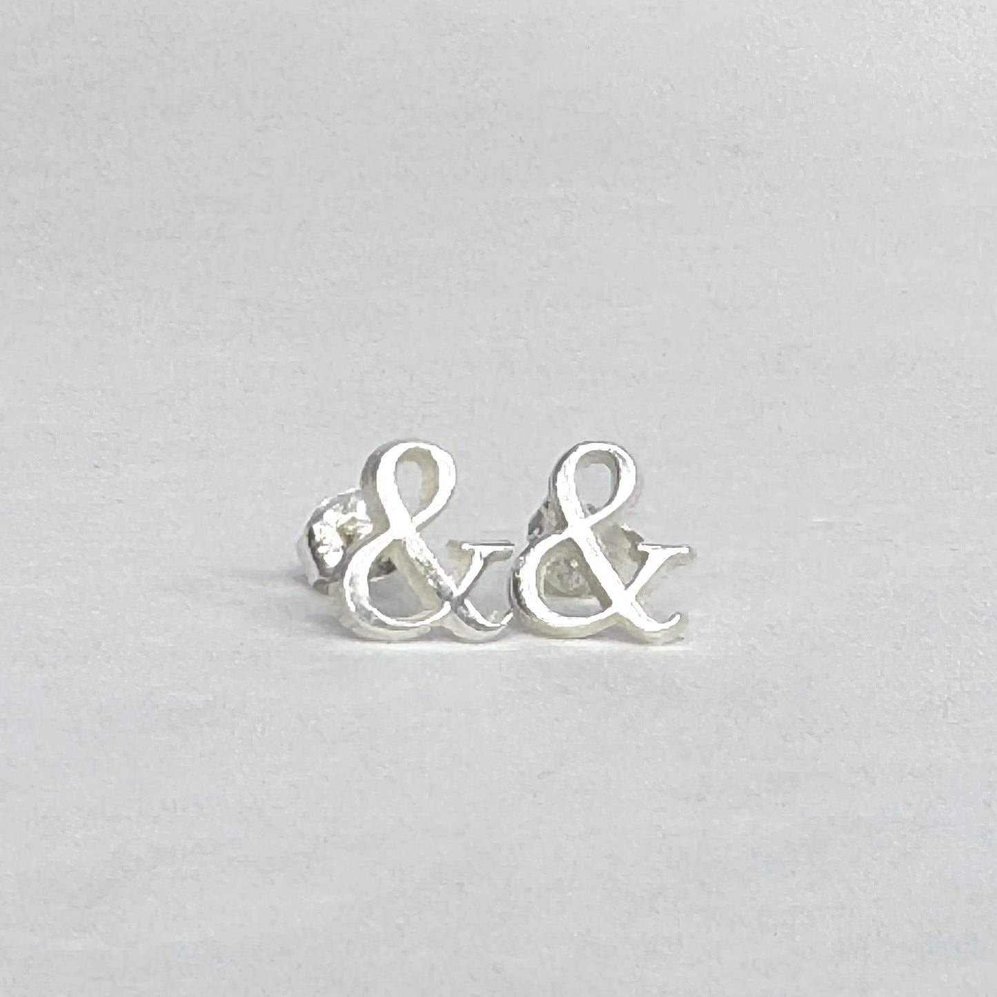 Sterling silver stud earrings shaped like ampersands on a light grey background