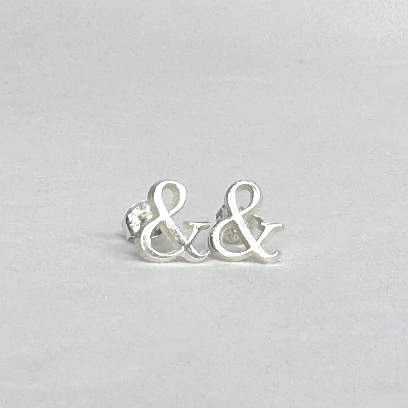 Sterling silver stud earrings shaped like ampersands on a light grey background