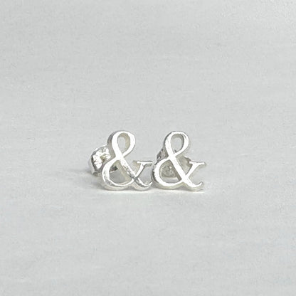 Sterling silver stud earrings shaped like ampersands on a light grey background