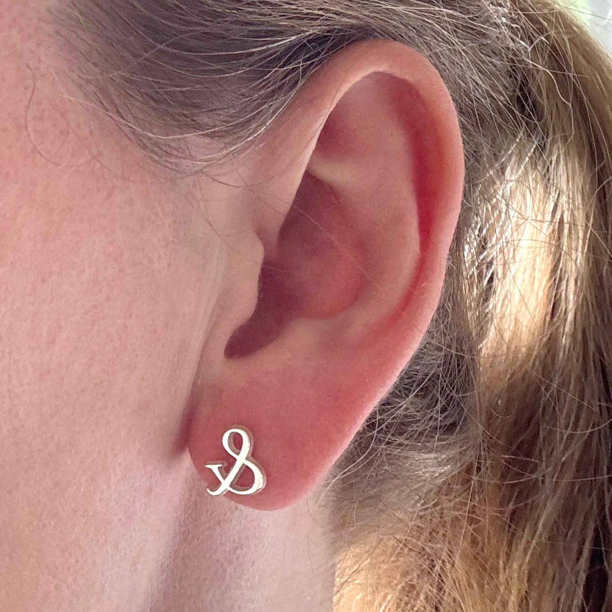 Close-up of an ear with a small sterling silver ampersand symbol stud earring.