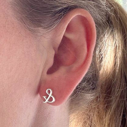 Close-up of an ear with a small sterling silver ampersand symbol stud earring.