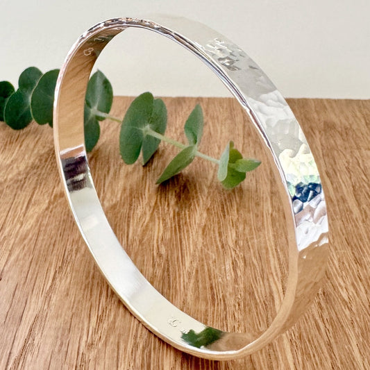 Hammered silver bangle on a wooden surface with a small sprig of eucalyptus leaves