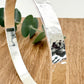 Hammered sterling silver bangle on a wooden surface with a small sprig of eucalyptus leaves