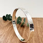 Hammered sterling silver bangle on a wooden surface with a small sprig of eucalyptus leaves