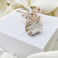Silver hoop earrings with hammered texture on a white box against a beige fabric background
