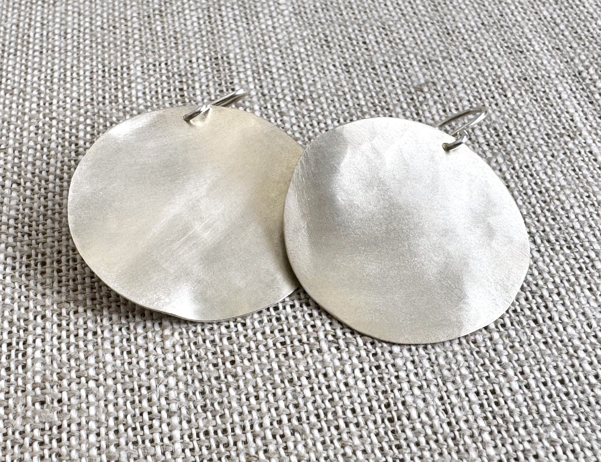 Pair of silver round earrings on a textured gray background
