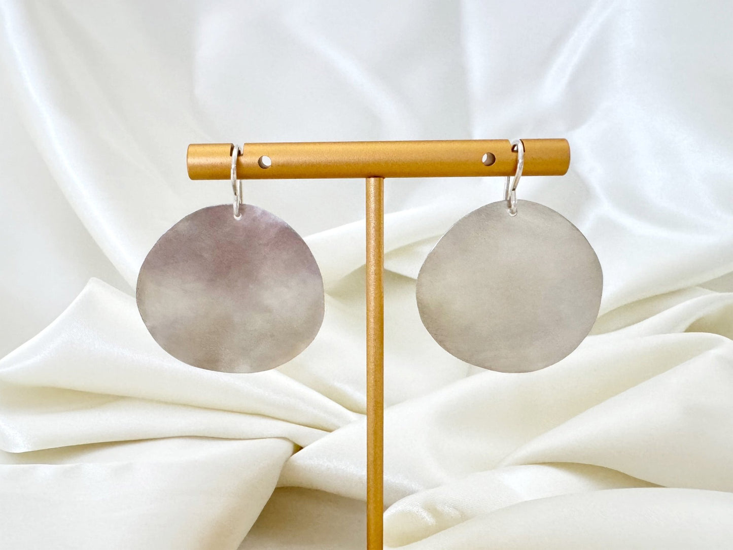 Pair of large hammered sterling silver disc earrings on a brass stand with a white fabric background