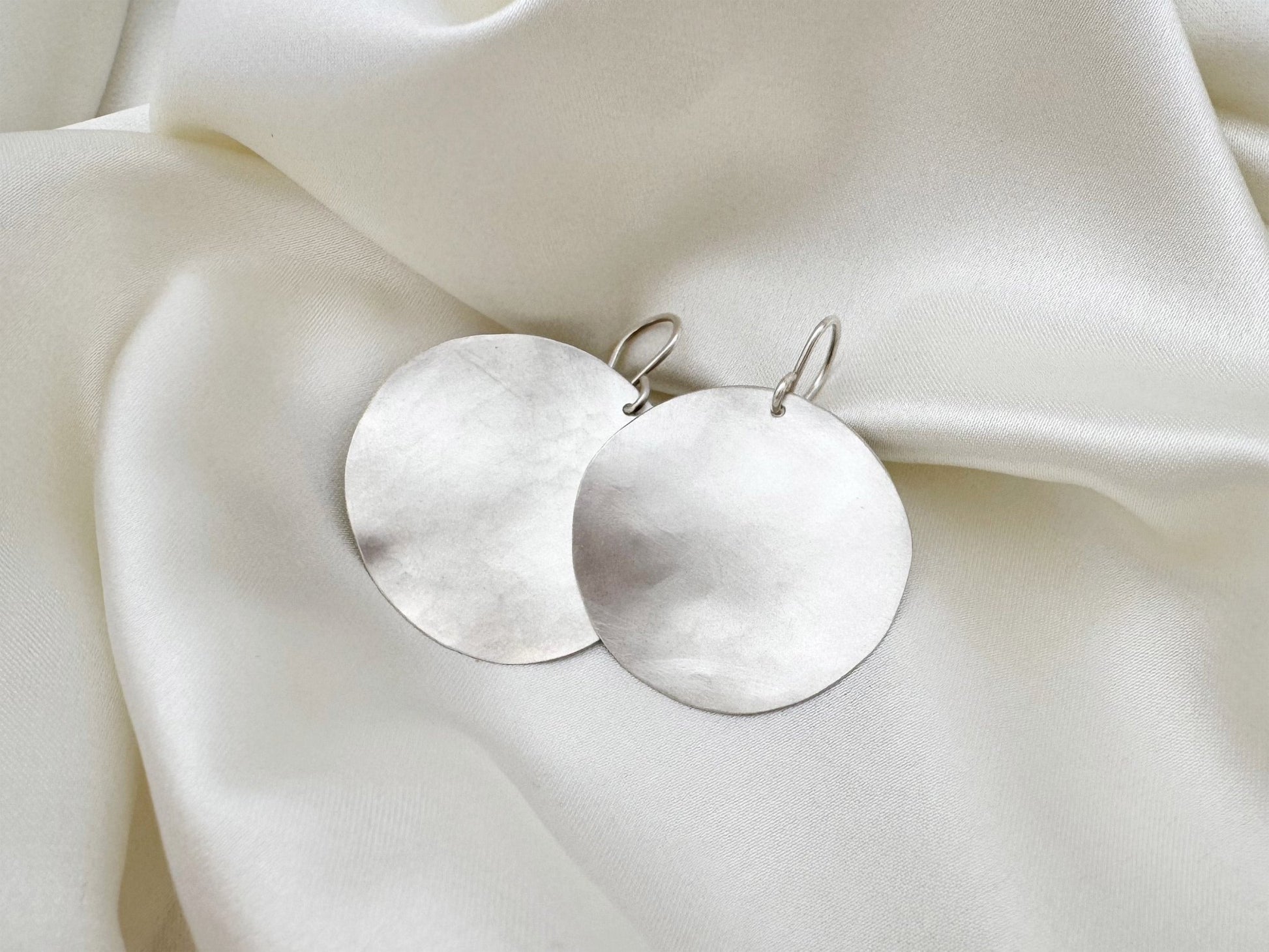 Silver earrings on a soft white fabric background