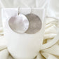 Silver circular earrings on a white cup with a white fabric background