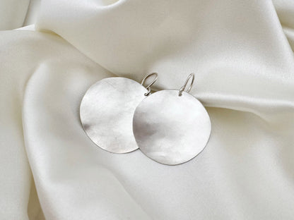 Silver earrings on a soft white fabric background
