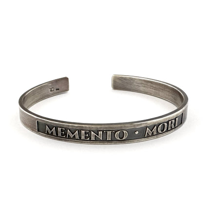 Memento mori cuff bracelet in oxidised sterling silver with raised MEMENTO MORI lettering