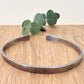 An oxidised sterling silver bracelet with flared ends on a wooden surface with eucalyptus leaves in the background.