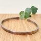 An oxidised sterling silver bracelet with flared ends on a wooden surface with eucalyptus leaves in the background.