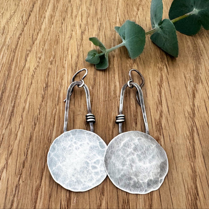 Silver earrings on a wooden surface with eucalyptus leaves.