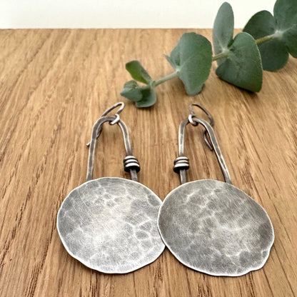 Pair of oxidised sterling silver earrings on a wooden surface with a sprig of eucalyptus.