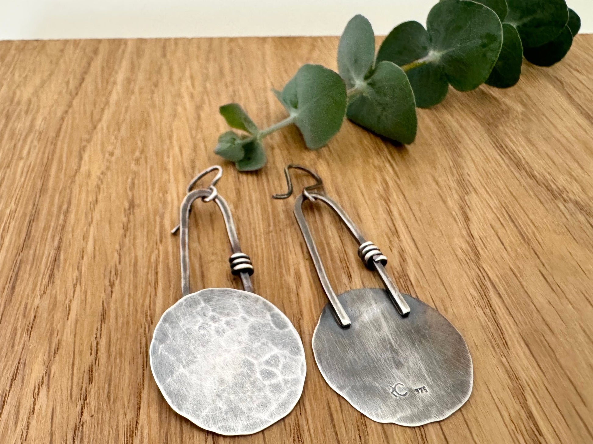 Pair of oxidised sterling silver earrings on a wooden surface with eucalyptus leaves.