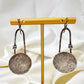 Pair of oxidised sterling silver statement earrings on a brass stand with a white fabric background.