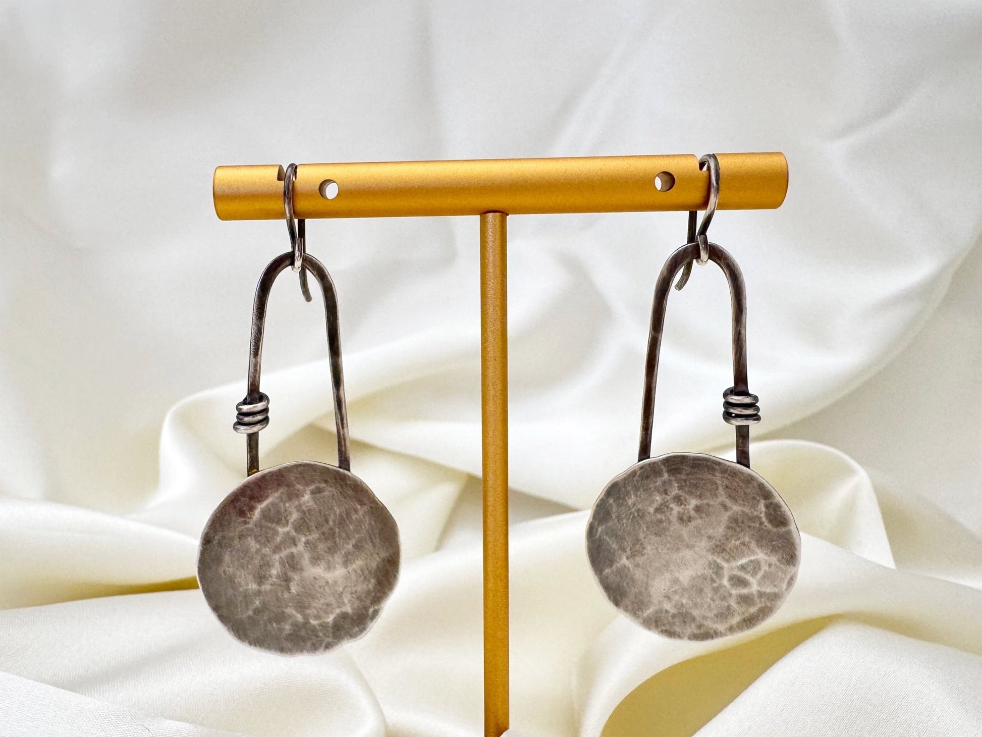 Pair of oxidised sterling silver statement earrings on a brass stand with a white fabric background.