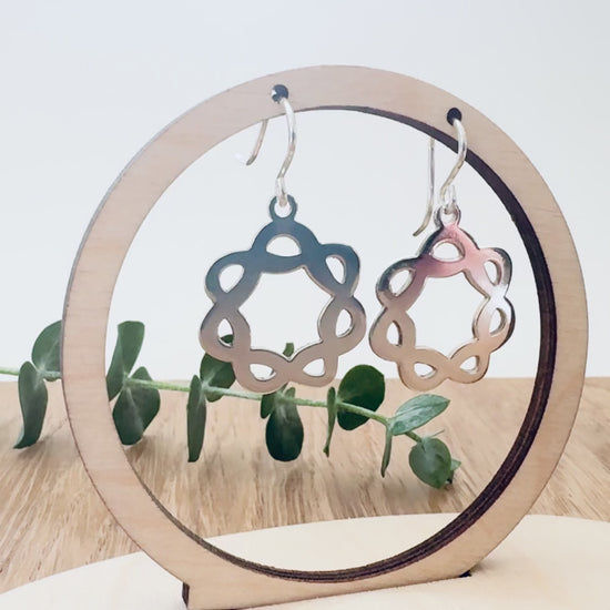Sterling silver celtic knot hoop earrings on a wooden surface with a small sprig of eucalyptus.