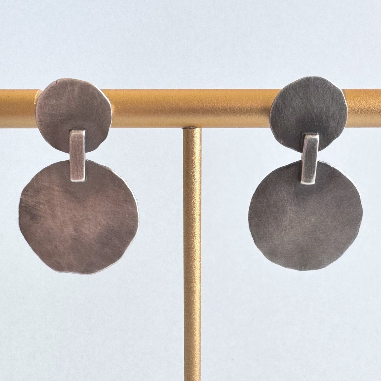 Pair of oxidised sterling silver earrings on a gold rod against a light blue background
