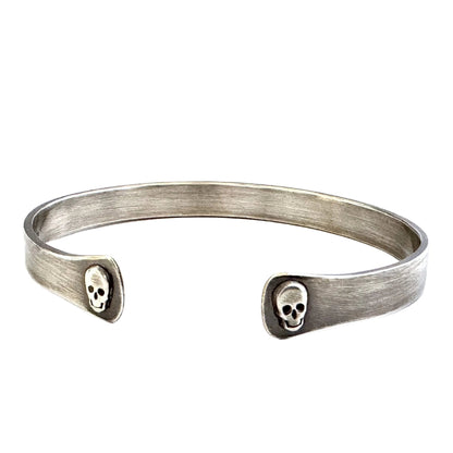 Oxidised sterling silver cuff bracelet with skull designs on a white background