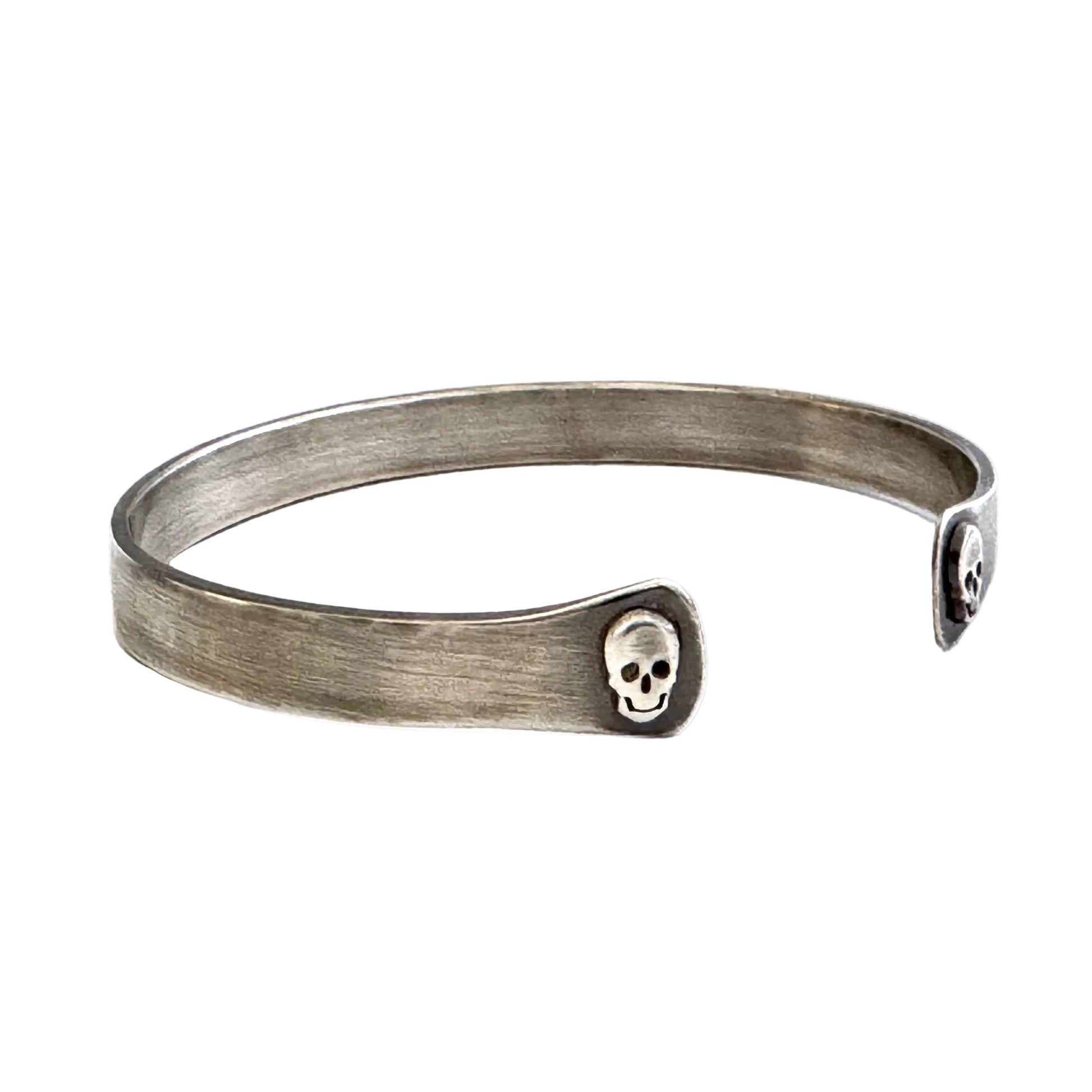 Oxidised sterling silver cuff bracelet with skull designs on a white background