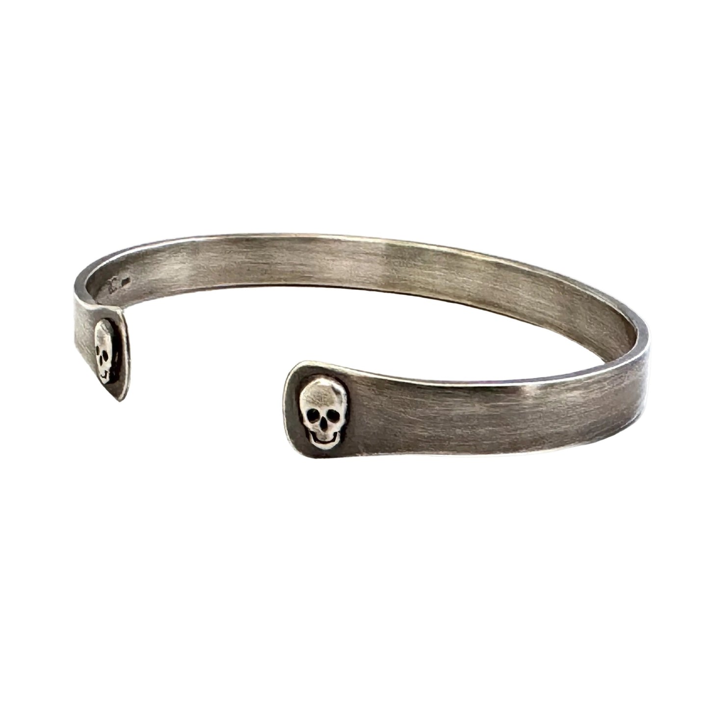 Oxidised sterling silver cuff bracelet with skull designs on a white background