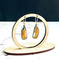 A pair of handmade sterling silver drop earrings featuring gold rutile quartz gemstones. The sterling silver bezel settings have been heavily oxidised and the earwires are 14k gold fill lever backs. The earrings are hanging from a wooden stand, which is on a white marble base with a black background.