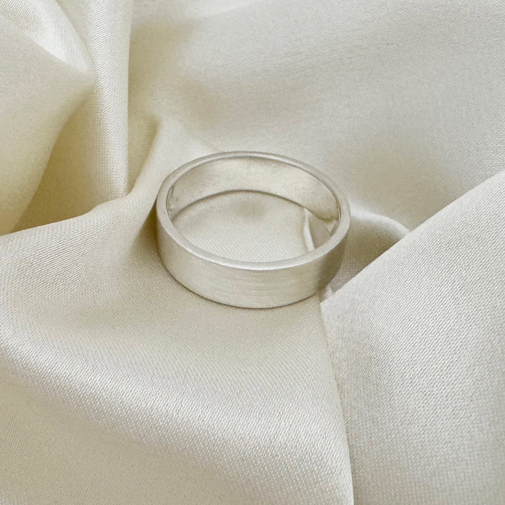 Flat sterling silver wedding ring with a brush finish against a cream satin background - Rebecca Cordingley Jewellery