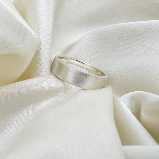 Flat sterling silver wedding ring with a brush finish against a cream satin background - Rebecca Cordingley Jewellery