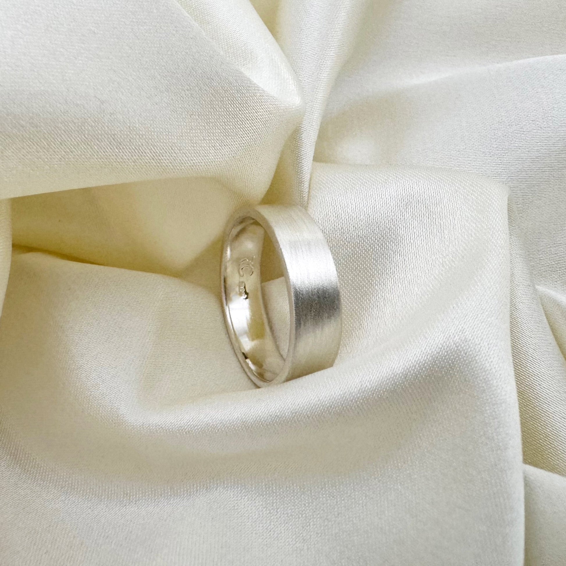 Flat sterling silver wedding ring with a brush finish against a cream satin background - Rebecca Cordingley Jewellery