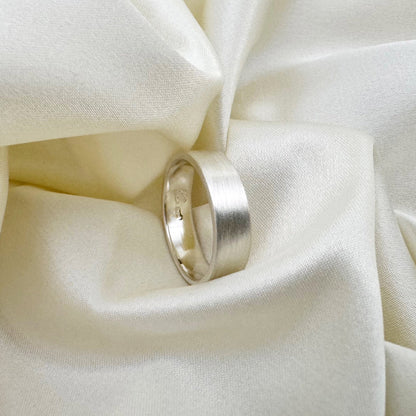 Flat sterling silver wedding ring with a brush finish against a cream satin background - Rebecca Cordingley Jewellery