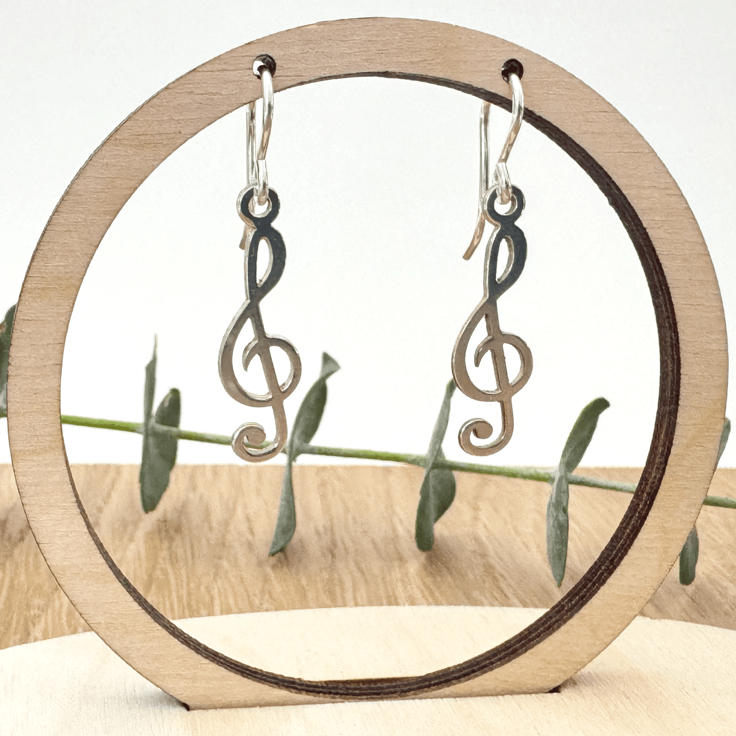 Silver treble clef earrings on a wooden stand with a natural background