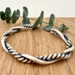 A sterling silver cuff bracelet on a wooden background with a small sprig of eucalyptus leaves. The cuff bracelet is comprised of two strands of silver, loosely twisted together. One is round and smooth, the other is very tightly twisted. It has been oxidised.