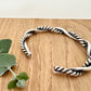 A sterling silver cuff bracelet on a wooden background with a small sprig of eucalyptus leaves. The cuff bracelet is comprised of two strands of silver, loosely twisted together. One is round and smooth, the other is very tightly twisted. It has been oxidised.