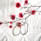 A pair of unique, abstract shaped sterling silver earrings, sitting on a textured white dish. There is dyed red blossom behind the earrings. Handmade by Australian jeweller Rebecca Cordingley.