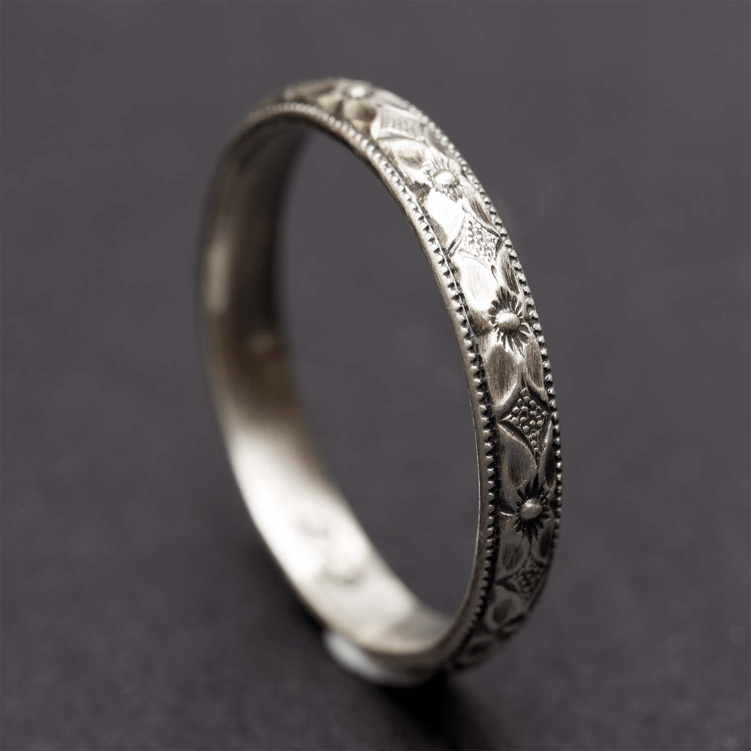 A sterling silver floral ring standing up on a dark grey background