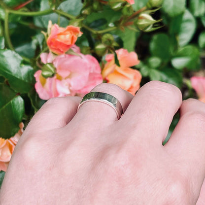 Square sterling silver wedding ring with bevelled edges, on ring finger in front of pink and apricot rose bush, handmade in Australia